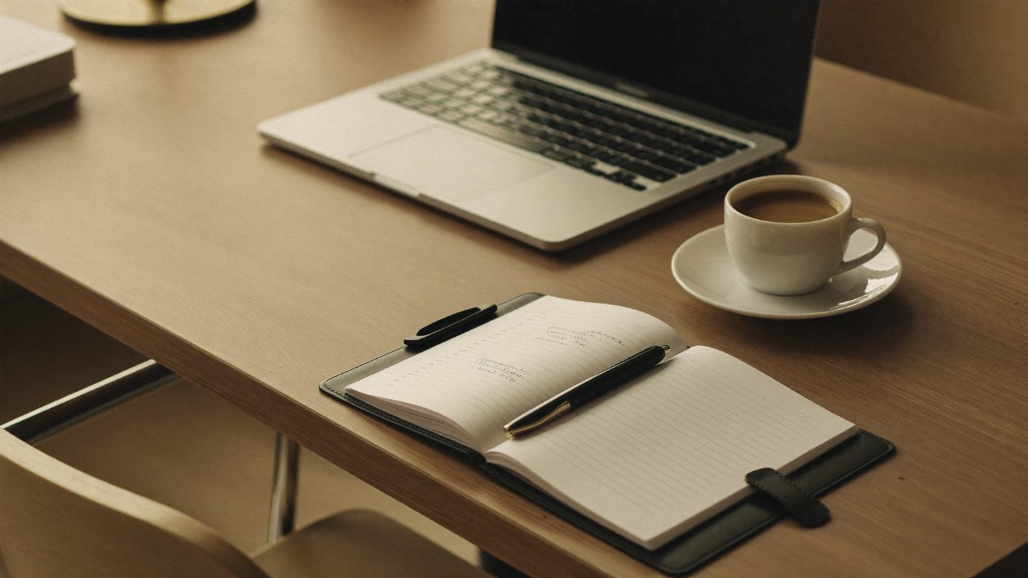 A tidy desk with a laptop, planner and coffee in warm light
