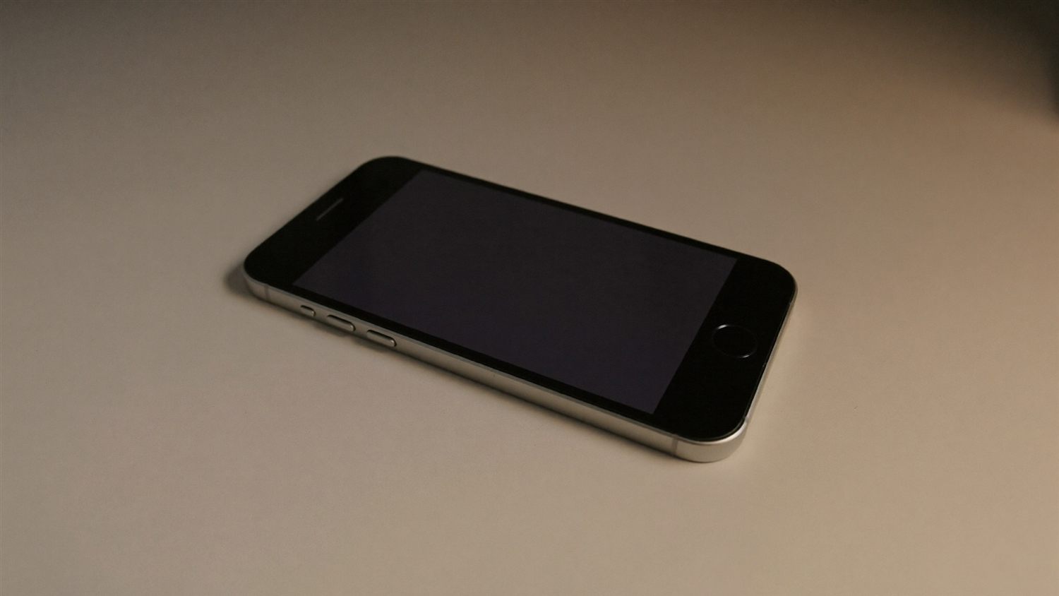 A smartphone lying face-up on a desk with a dark, silent screen